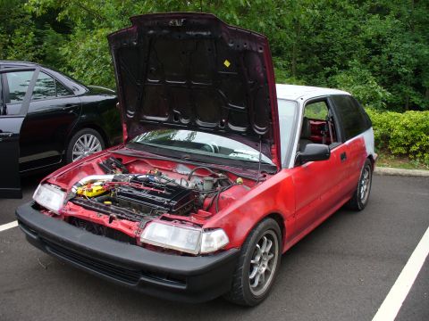 1991 Ford Probe - A red hatchback is shown with its hood open, revealing the engine compartment. Another vehicle is visible to the left.