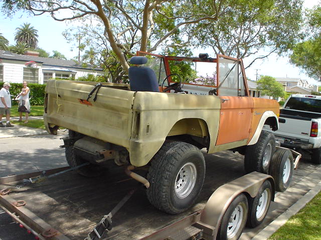 1977 Ford Bronco on trailer, orange and tan, missing parts, with white pickup truck behind