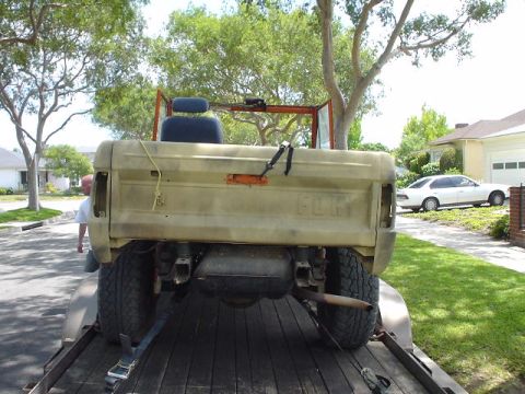 1977 Ford Bronco - The rear of a tan 1977 Ford Bronco is visible, with the 'FORD' lettering clearly stamped on the tailgate.