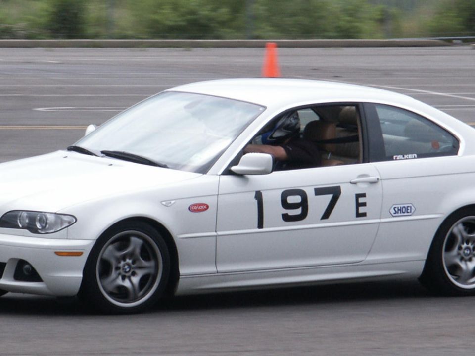 White BMW coupe with racing numbers '197E' on the side, driving on a track with an orange cone nearby