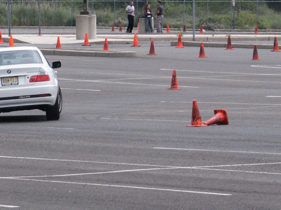 White BMW sedan with license plate RAN-51J in a parking lot set up for a driving course with orange cones