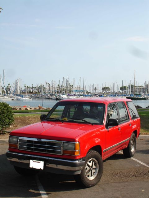 1992 Ford Explorer - A red 1992 Ford Explorer is parked near a marina filled with sailboats.