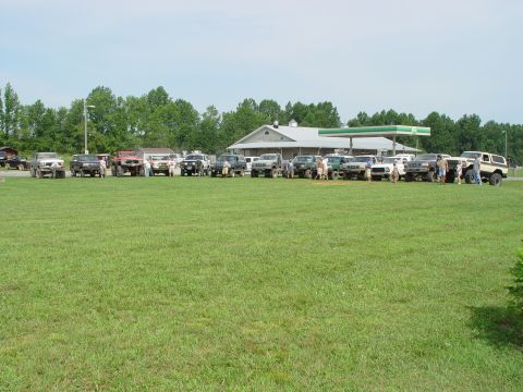 1996 Ford Bronco - A collection of SUVs and trucks are gathered in a grassy field near a gas station.