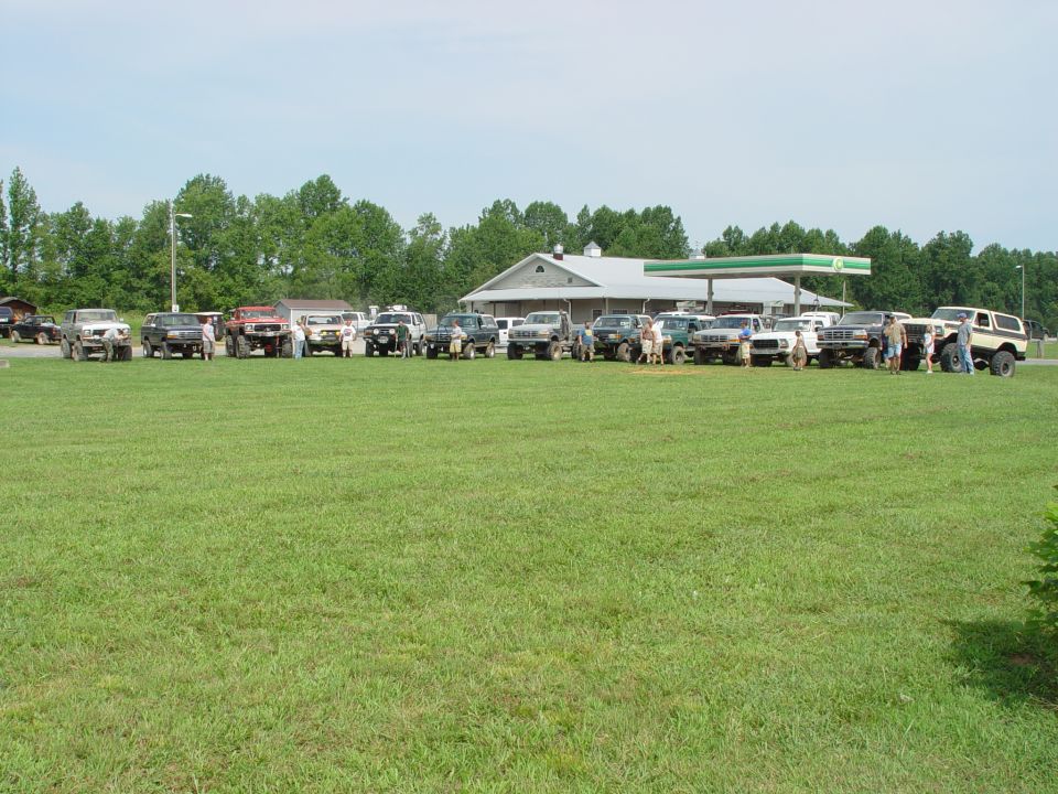 Group of SUVs and trucks parked on grass, with a gas station in the background
