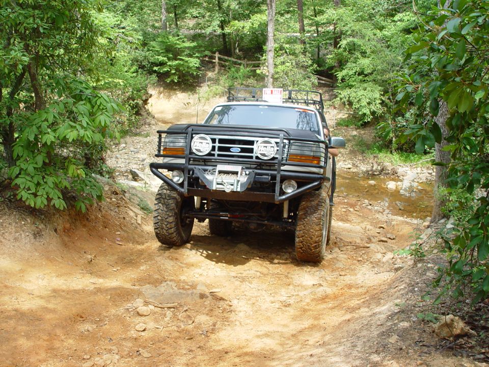 1996 Ford Bronco with aftermarket bumper and winch driving on a muddy trail