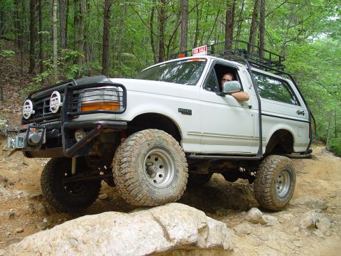 1996 Ford Bronco - This modified Ford Bronco navigates a rocky trail, with a 'For Sale' sign visible on its roof rack.