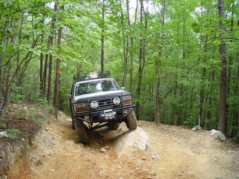 1996 Ford Bronco - A white Ford Bronco navigates a challenging rocky path through a dense forest.