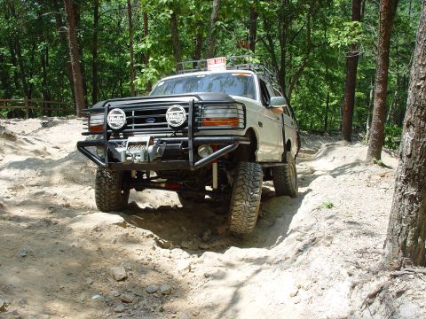 1996 Ford Bronco - This 1996 Ford Bronco is navigating a challenging off-road trail in a wooded area.
