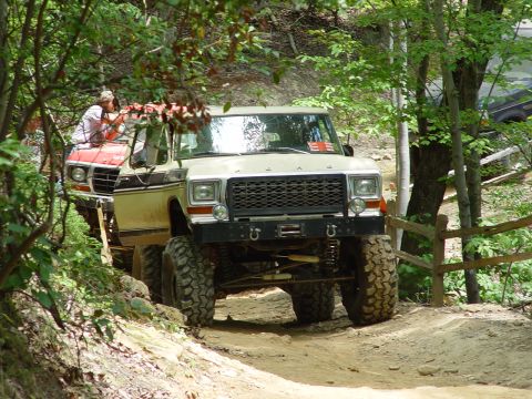 1996 Ford Bronco - Two trucks navigate a wooded trail, one with large tires and a winch.
