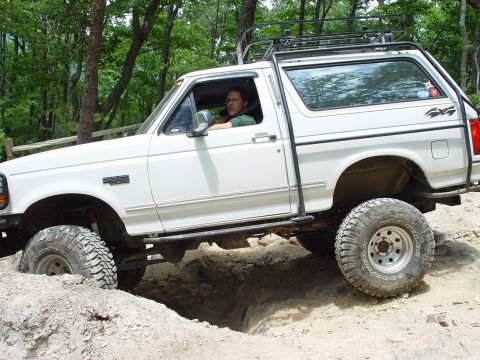 1996 Ford Bronco - A white Ford Bronco navigates a challenging off-road terrain with a driver inside.