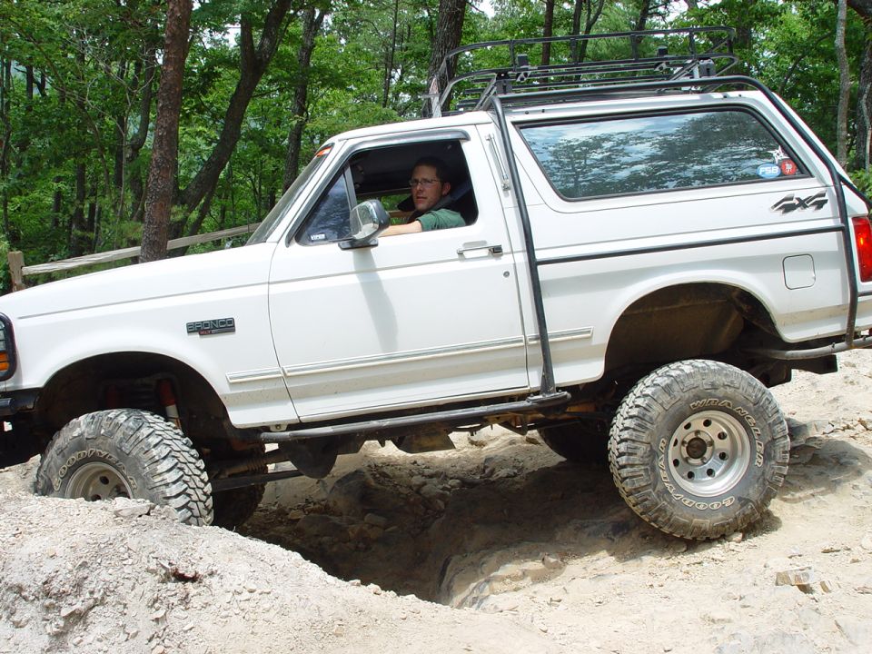 White Ford Bronco with roof rack driving off-road, front 3/4 view