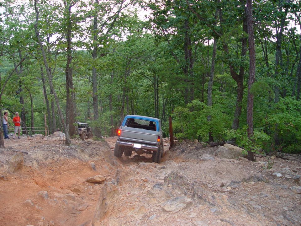 1996 Ford Bronco navigating a steep, rocky off-road trail with another vehicle visible in the background