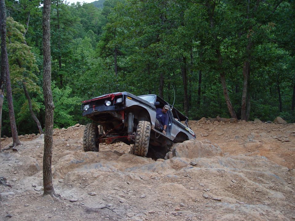 Dark gray Ford Bronco off-roading on a rocky hill, driver visible in open door