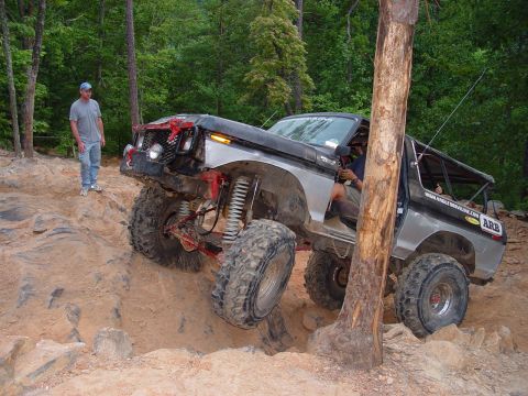 1996 Ford Bronco - This heavily modified SUV is navigating a challenging off-road obstacle course with a spectator observing.