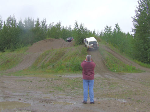 Man photographing a white-topped 4x4 descending a steep dirt hill climb