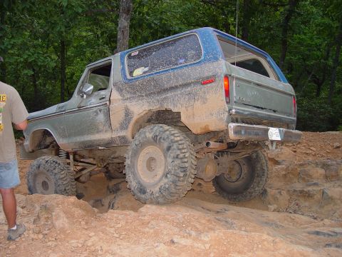 1996 Ford Bronco - This lifted Ford Bronco is navigating a challenging off-road course with significant mud and rock obstacles.