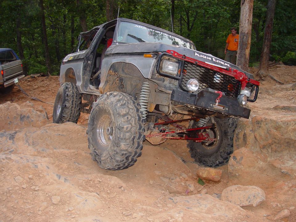 Gray primered lifted Ford Bronco rock crawler climbing rocks on a wooded trail