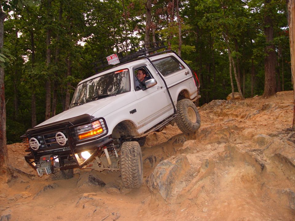 White lifted Bronco with brush guard and winch crawling down a rock ledge trail