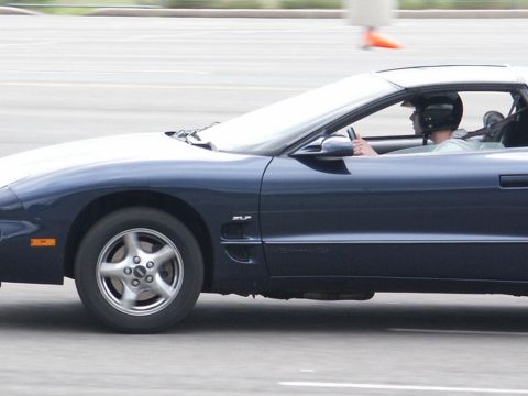 2001 Mercury Grand Marquis - Side view of a dark blue Pontiac Firebird coupe with SLP badging, driver wearing a helmet.