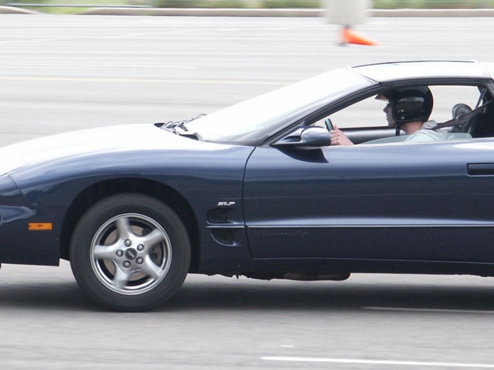 Dark blue Pontiac Firebird coupe driving, driver wearing helmet. SLP badging visible