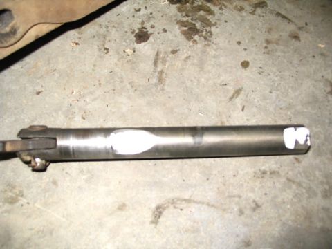 1978 Ford Bronco - A close-up view of a metal driveshaft component, marked with white paint, resting on a concrete surface.