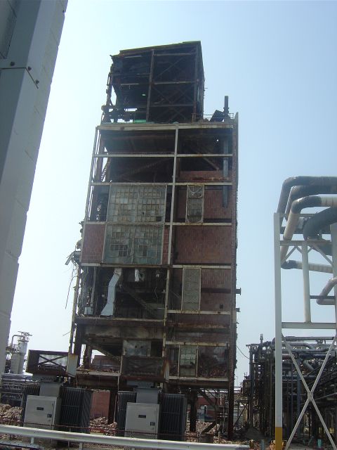 1987 Suzuki Samurai - The skeletal remains of a multi-story industrial structure stand against a clear sky, showing extensive damage.