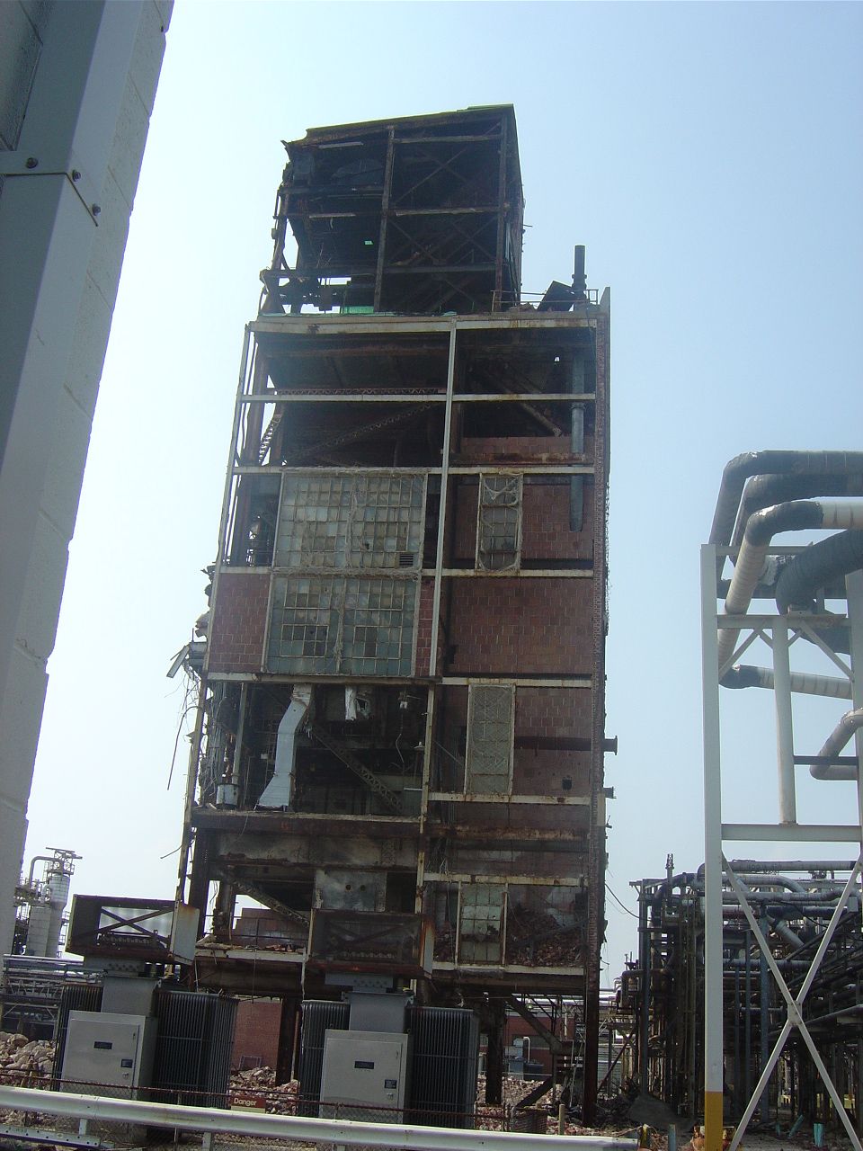 tall, damaged industrial building with exposed metal frame and broken windows, pipes on the right