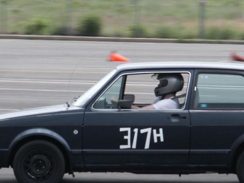 2001 Mercury Grand Marquis - A driver in a helmet races a dark hatchback with large white numbers on its side.