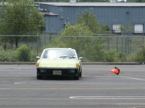 2001 Mercury Grand Marquis - A yellow sports car drives on a paved lot with an orange cone nearby.