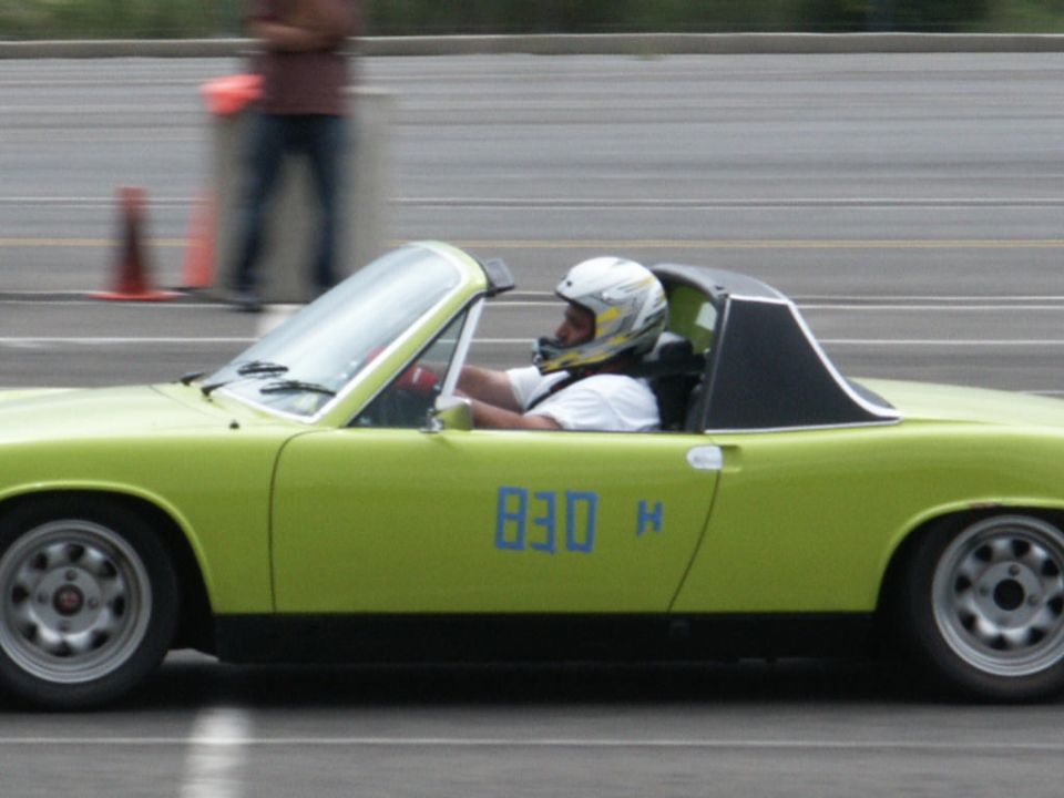 Lime green convertible sports car with blue racing numbers '830 H' on the door, driver wearing a helmet