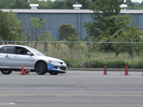 2001 Mercury Grand Marquis - A silver Mitsubishi Lancer Evolution navigates a course marked by orange cones, with a building and trees in the background.