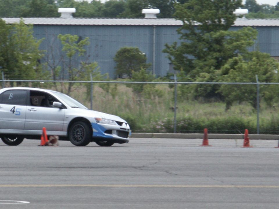 Silver Mitsubishi Lancer Evolution with blue front bumper accents and number 45 on the door, driving on a track with orange cones