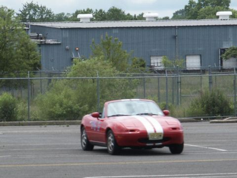 2001 Mercury Grand Marquis - A red convertible sports car with white racing stripes is seen from the front-right in an empty parking lot.