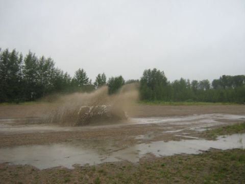 1995 Ford Bronco - A white SUV splashes through a muddy track surrounded by trees under an overcast sky.