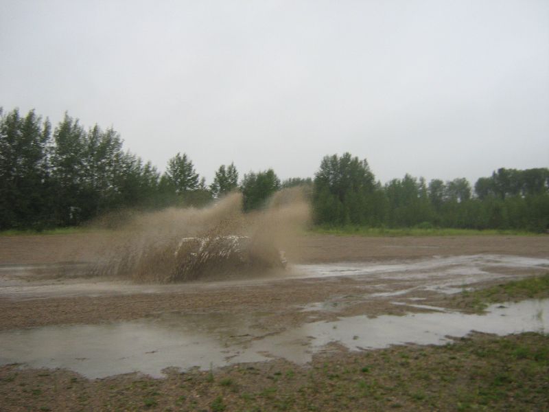 White SUV kicking up mud while driving through a puddle