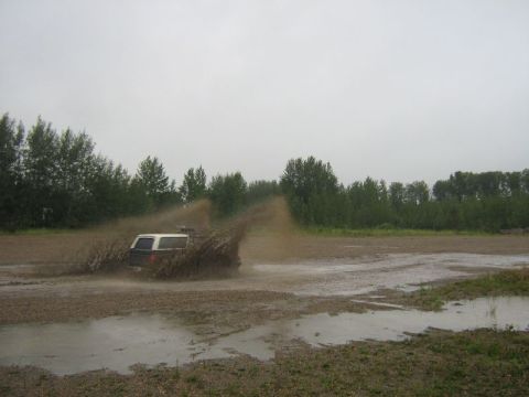 1995 Ford Bronco - A 1995 Ford Bronco navigates a muddy track, sending a spray of dirt and water into the air.