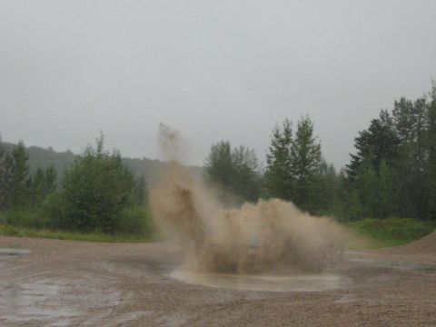 1995 Ford Bronco - A 1995 Ford Bronco navigates a wet, gravelly terrain, creating a significant water and dirt spray.