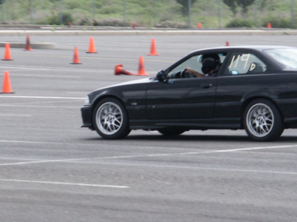 Black coupe with racing number 119 on door, driving on a track with cones