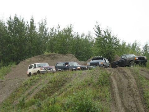 1995 Ford Bronco - Several off-road vehicles navigate a challenging dirt terrain under an overcast sky.