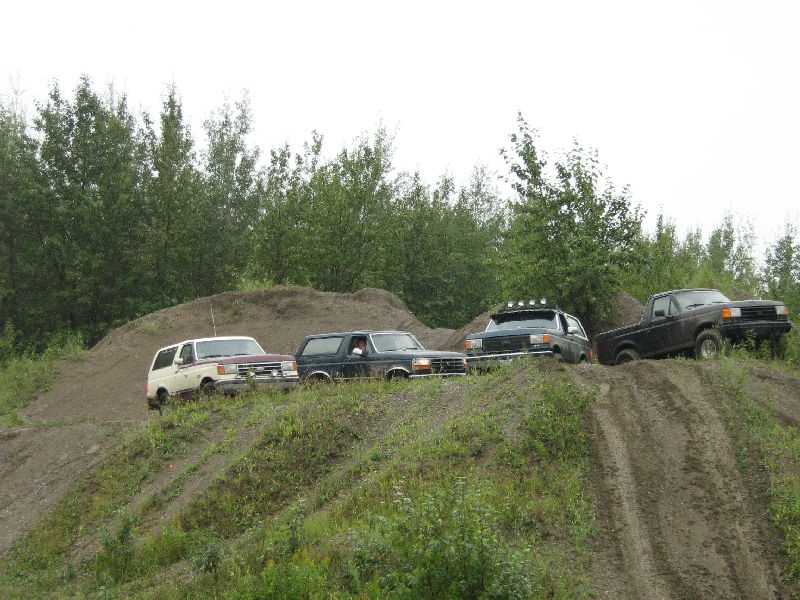 Four SUVs and a pickup truck drive on dirt hills with trees in the background