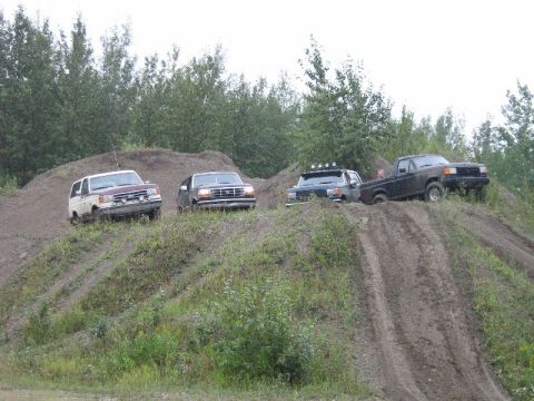 1995 Ford Bronco - Multiple trucks, including a 1995 Ford Bronco, navigate a challenging dirt hill climb.
