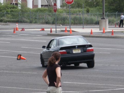 2001 Mercury Grand Marquis - A black BMW M3 coupe navigates a course marked by orange cones, with a woman observing in the foreground.