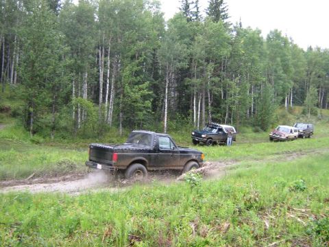 1995 Ford Bronco - Four-wheel drive vehicles navigate a muddy trail through a forest.