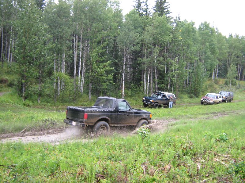 1995 Ford Bronco driving through mud on a dirt road, other SUVs in background