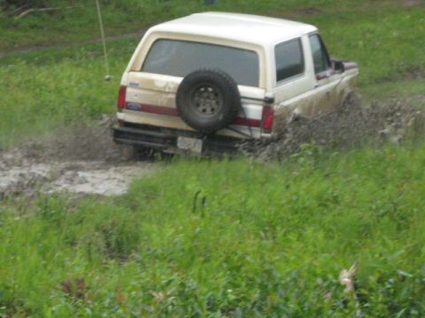 1995 Ford Bronco - A white Ford Bronco navigates a muddy off-road course, kicking up dirt and water.
