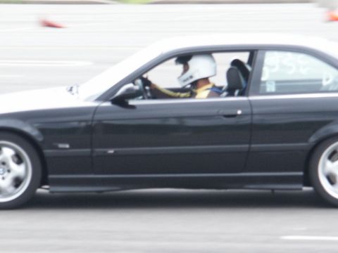 2001 Mercury Grand Marquis - A driver in a helmet navigates a turn on a race track in a black coupe.