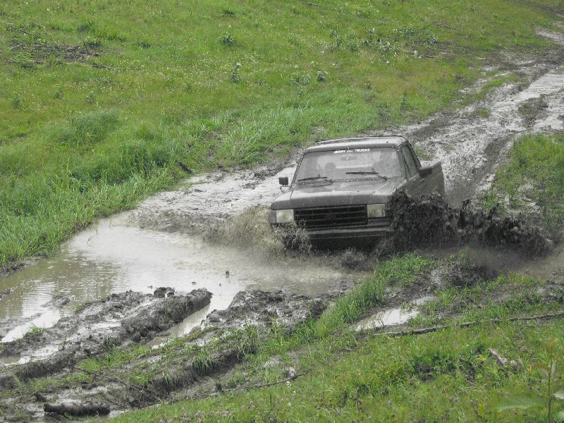 Dark colored pickup truck splashing through a muddy track with grass on either side