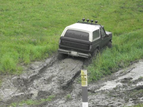1995 Ford Bronco - A 1995 Ford Bronco navigates a challenging muddy terrain, passing a warning sign for an oil pipeline crossing.