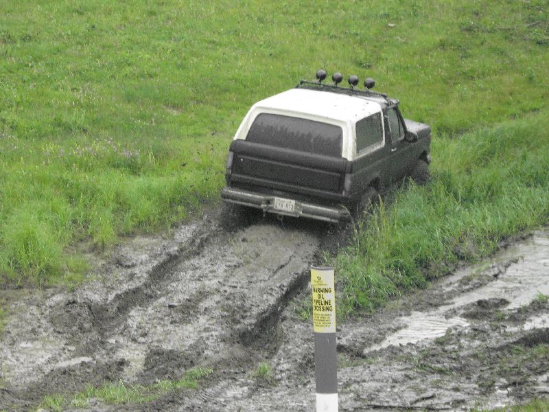 Ford Bronco driving through a muddy field with a pipeline crossing sign