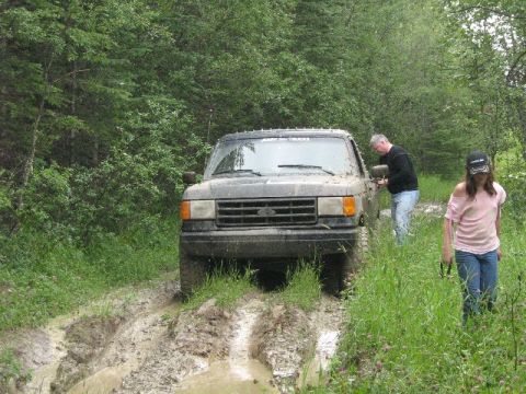 1995 Ford Bronco - A 1995 Ford Bronco navigates a muddy trail with two people nearby.